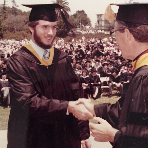 Older photo of alumnus Tim Baumgartner in cap and gown shaking hands